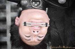 Dark-haired Asian hangs upside down in leather straitjacket